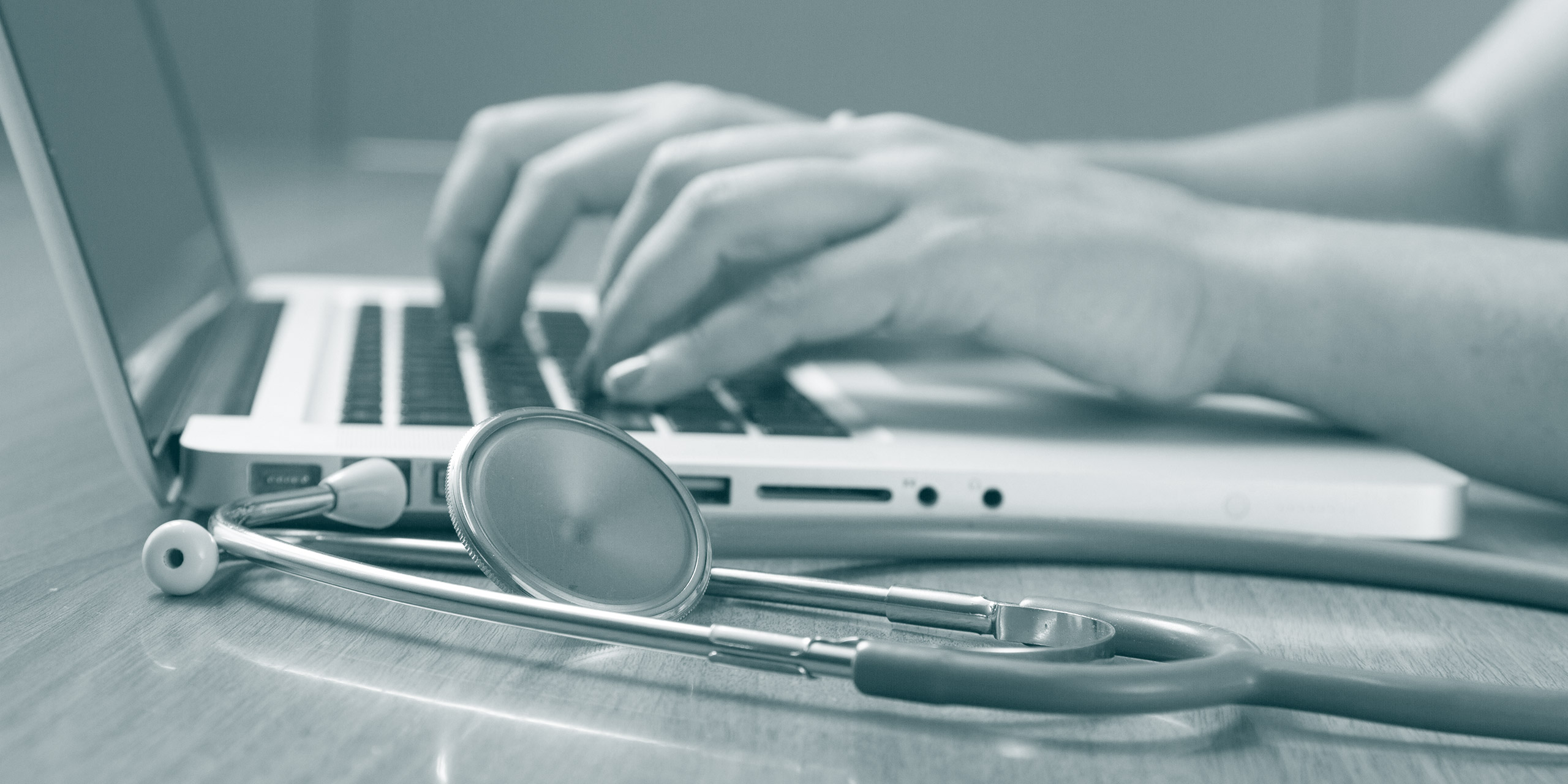 weibliche Hände die etwas an einem Laptop eintippen daneben liegt ein Stethoskop